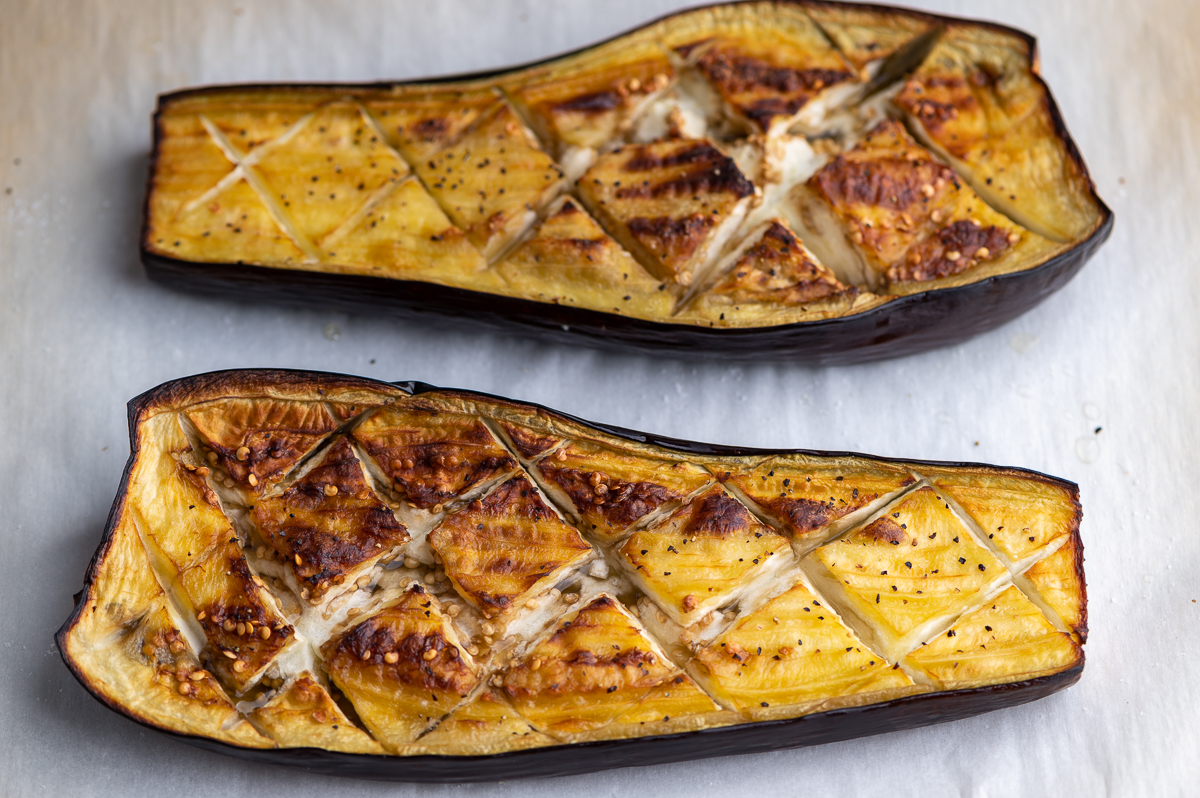 Eggplant halves brushed with olive oil and sprinkled with salt on a rimmed baking sheet in a home kitchen