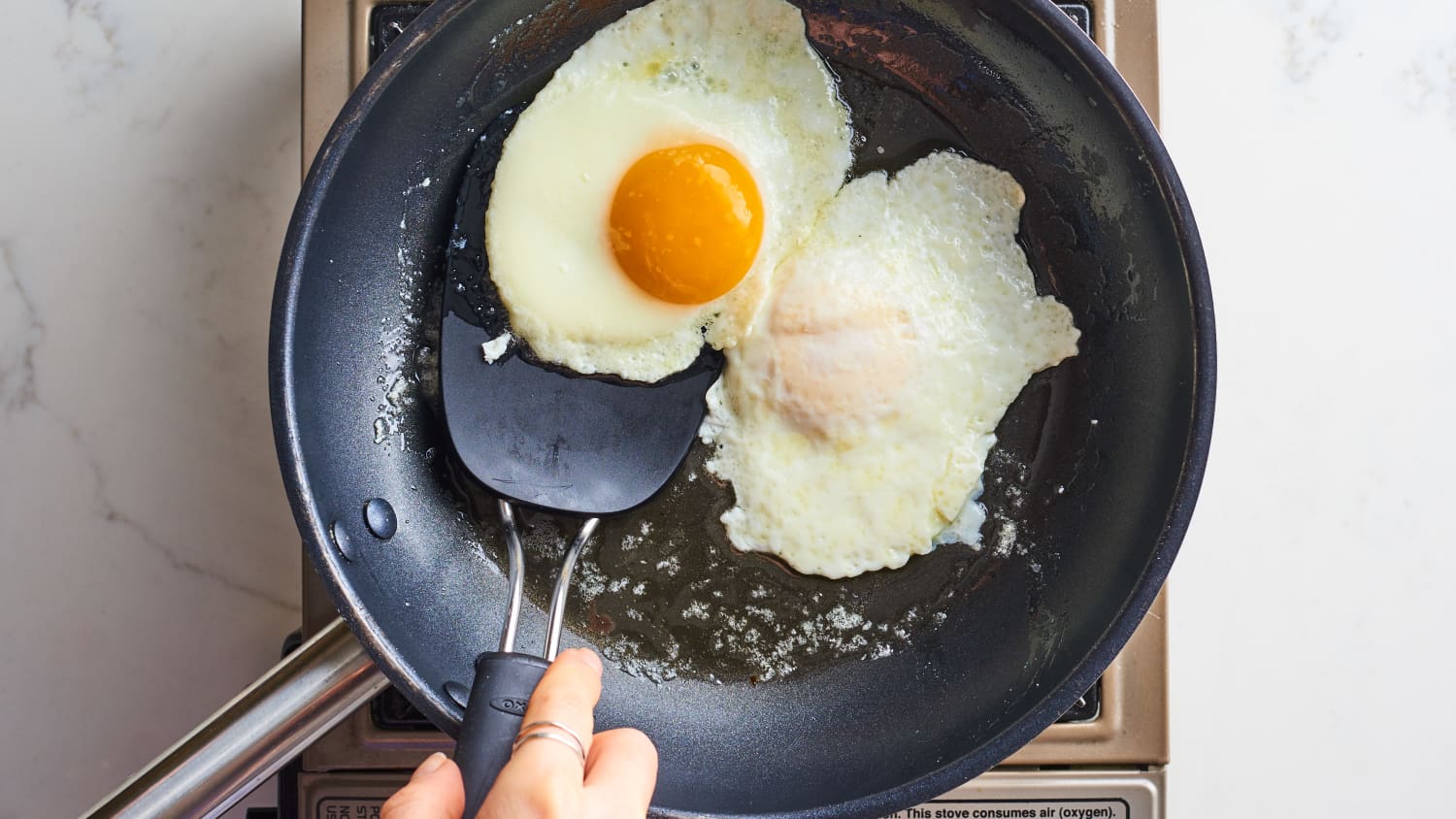 Eggs cracked into wells on top of a potato and sausage breakfast skillet, with a lid nearby on a stovetop