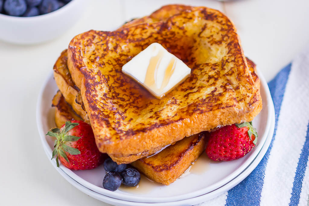 Eggs, milk, vanilla, cinnamon, butter, and thick slices of brioche arranged on a kitchen counter
