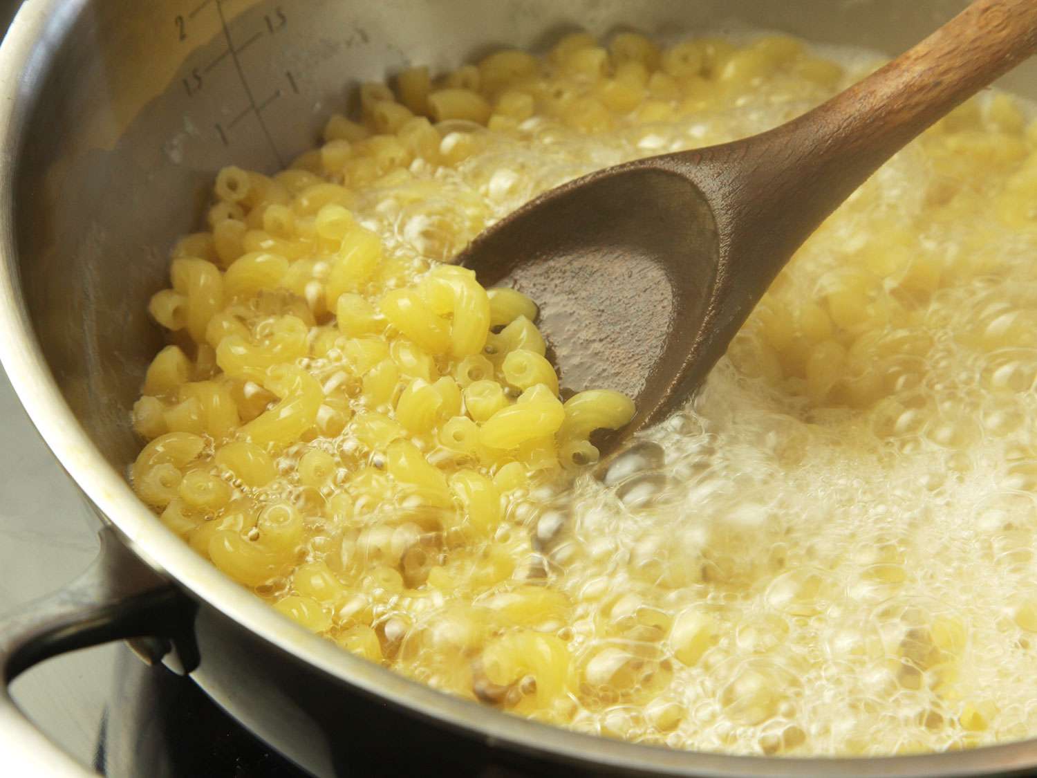 Elbow macaroni boiling in a large stainless steel pot on a stovetop with steam rising