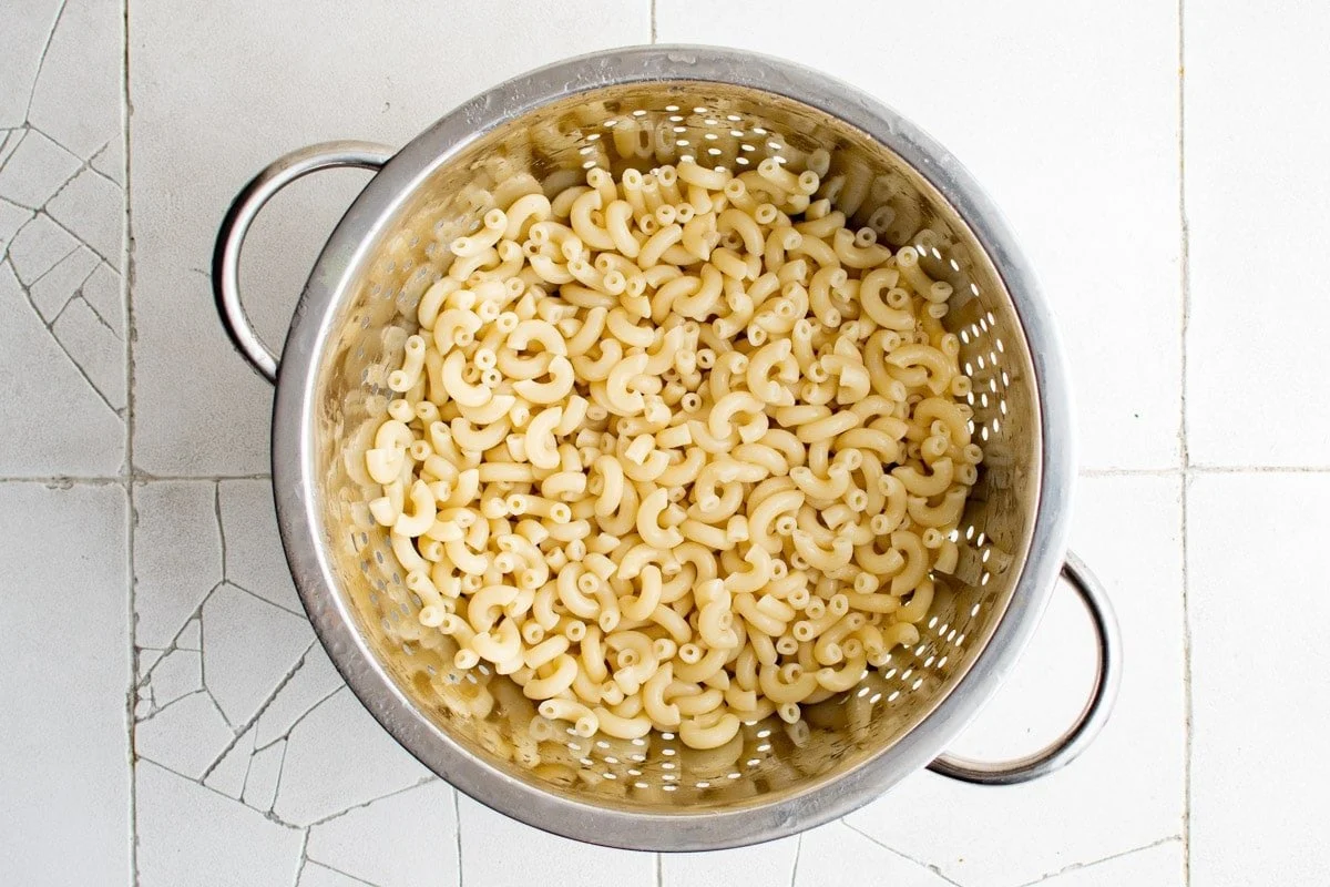 Elbow macaroni draining in a metal colander in a sink with steam rising