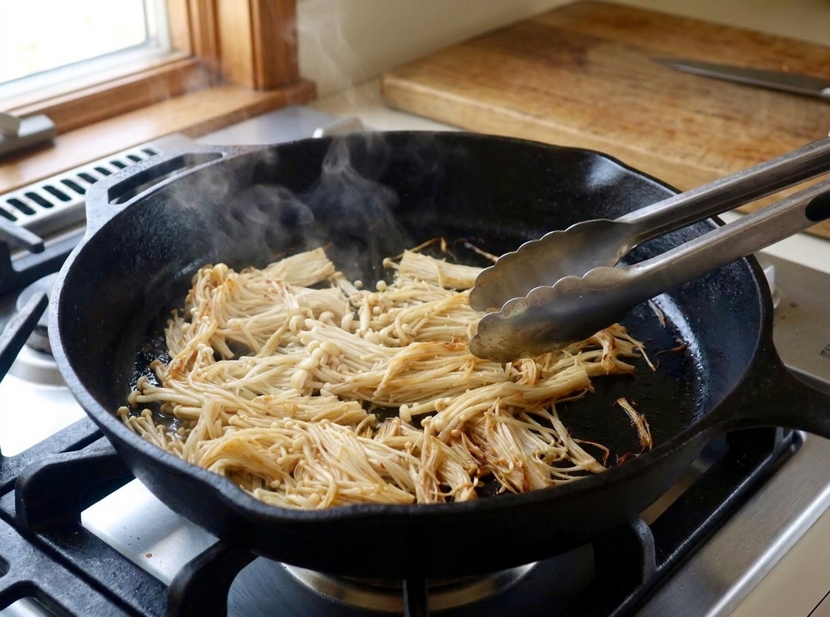 Enoki mushroom bundles browning in a hot skillet as they begin to turn golden at the edges