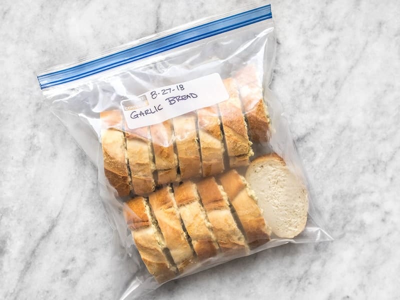 Even slices of homemade sandwich bread being placed into a freezer-safe zip-top bag on a kitchen counter
