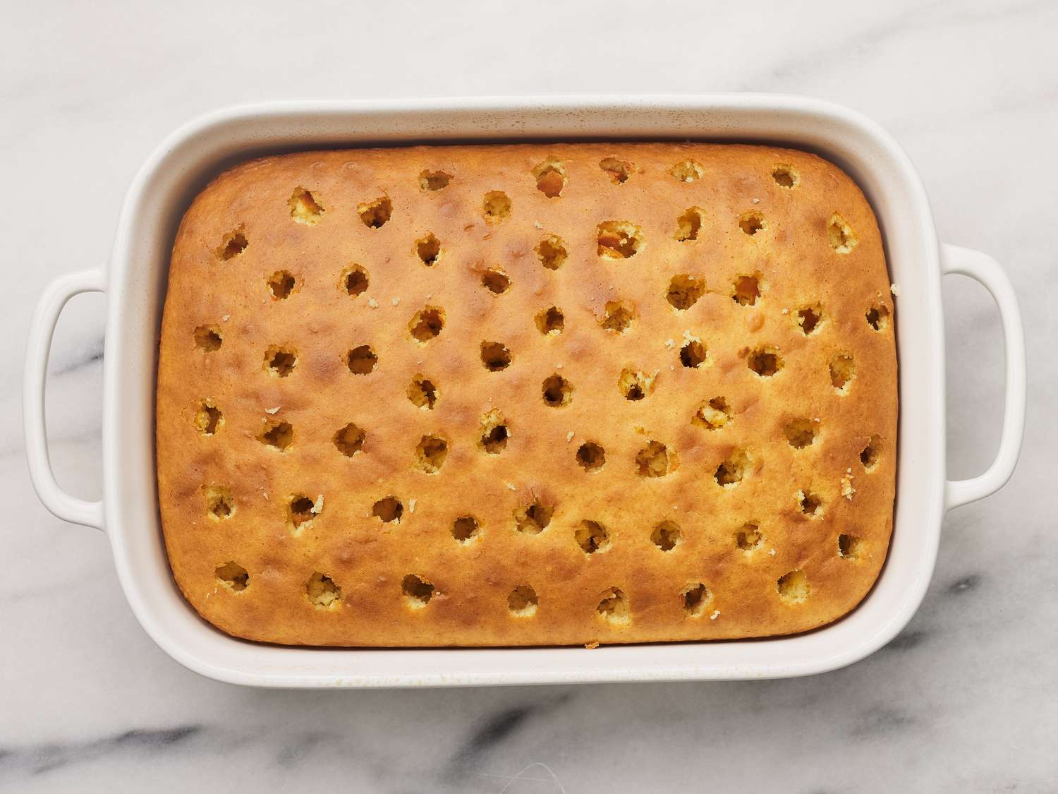 Evenly spaced holes poked into a warm sheet cake in a 9x13 pan using the handle of a wooden spoon