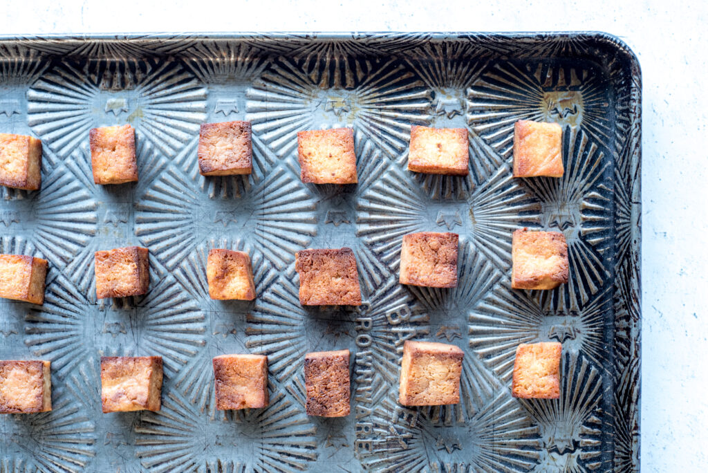 Evenly spaced tofu cubes on a parchment-lined sheet pan ready to be baked in a home kitchen