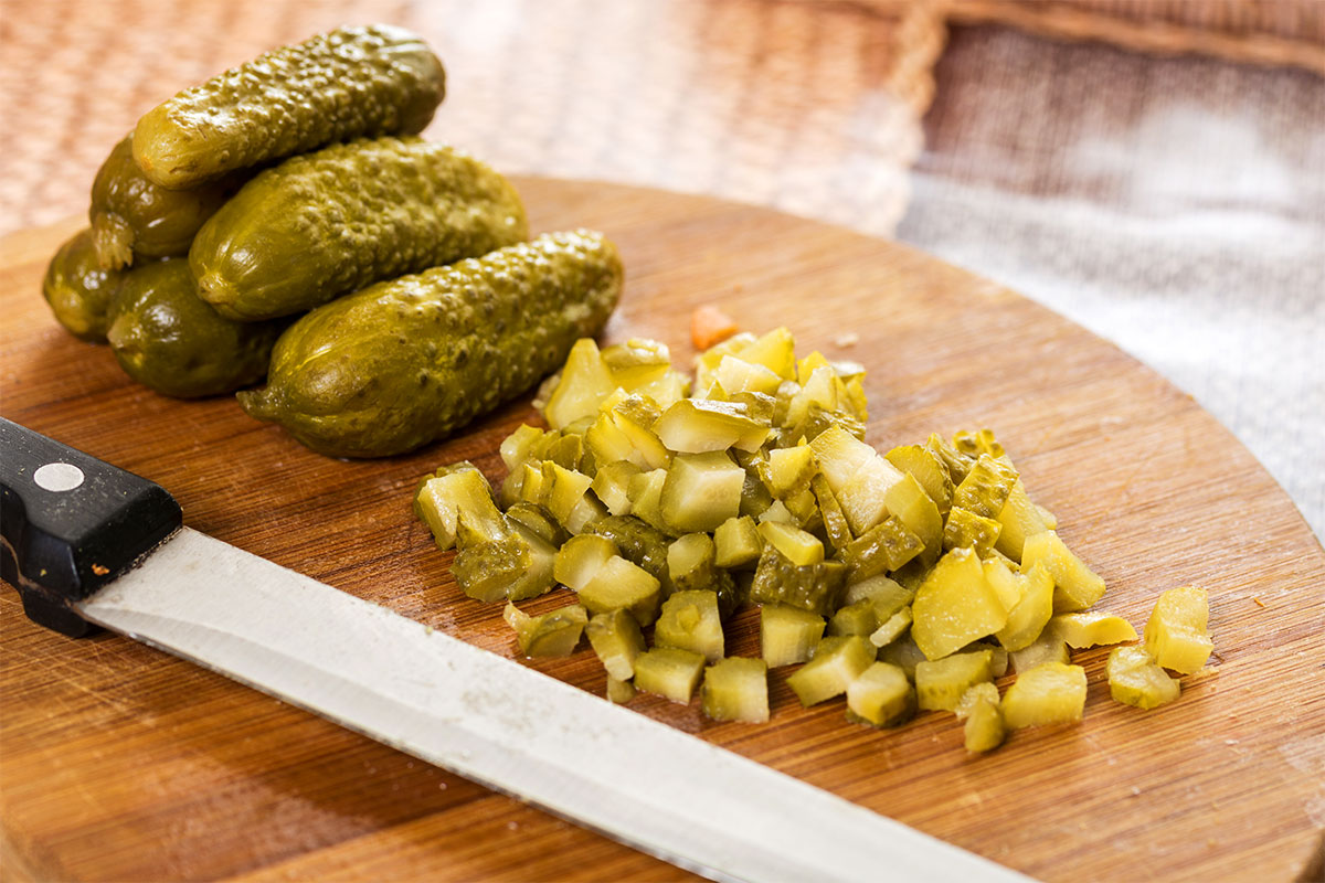 Finely chopped dill pickles on a wooden cutting board, ready to be patted dry