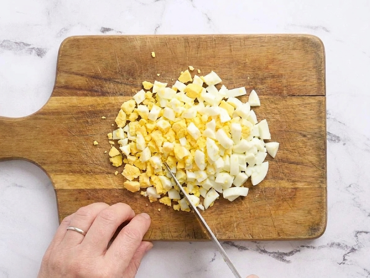 Finely chopped hard-boiled eggs on a cutting board ready to be added to chicken salad