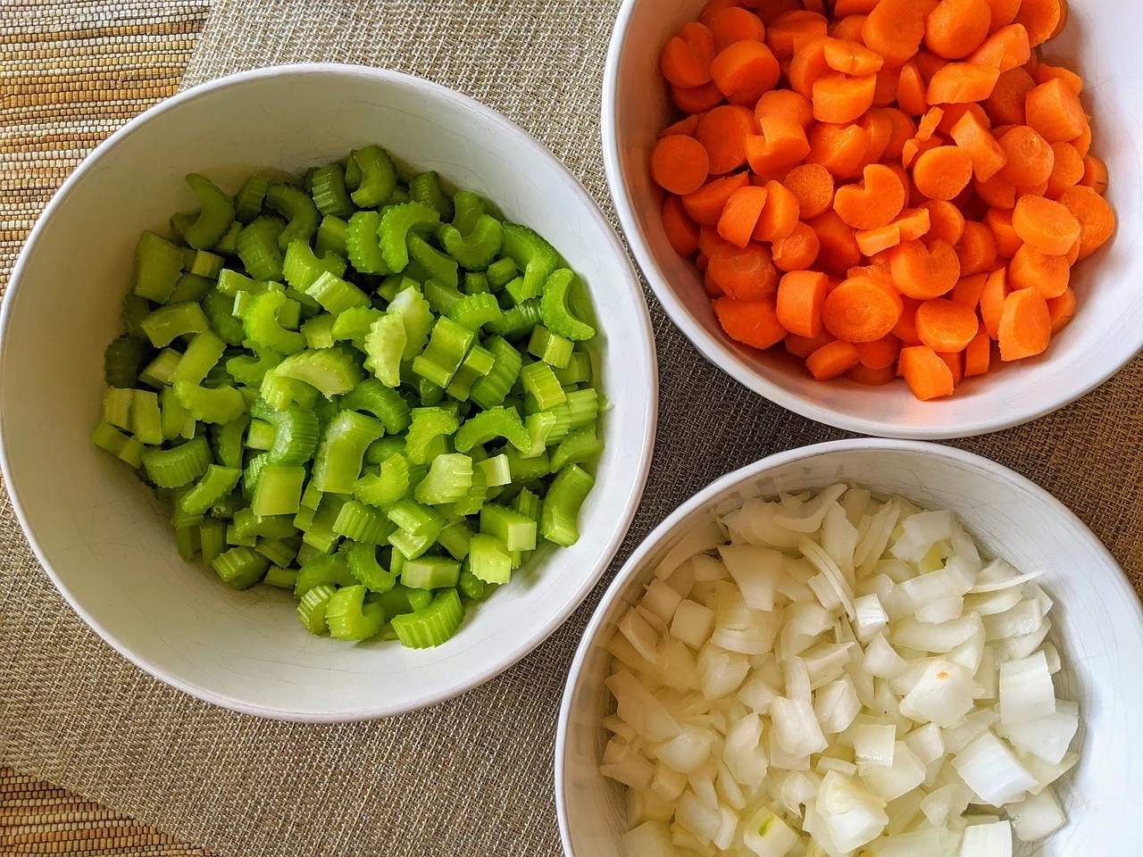 Finely chopped onion, carrot, and celery in small bowls on a kitchen counter ready for cooking