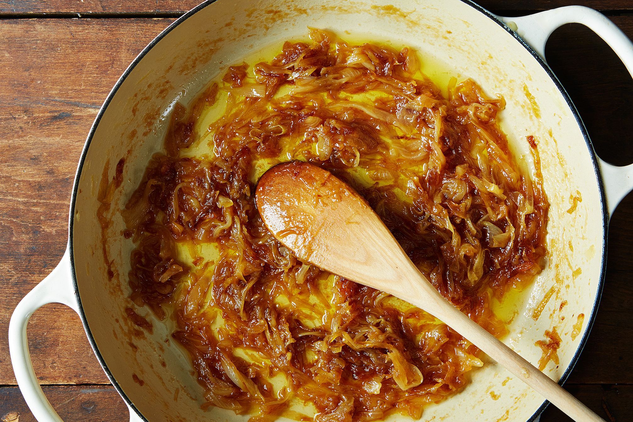 Finely chopped onions turning deep golden in a pot as a wooden spoon stirs on a stovetop