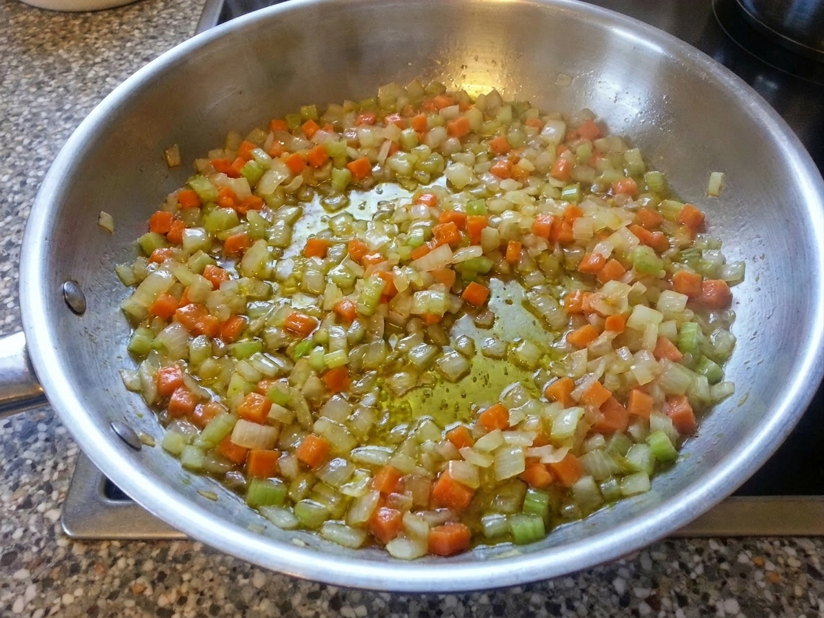 Finely diced onion, carrot, and celery cooking in olive oil in a wide skillet until softened and glossy