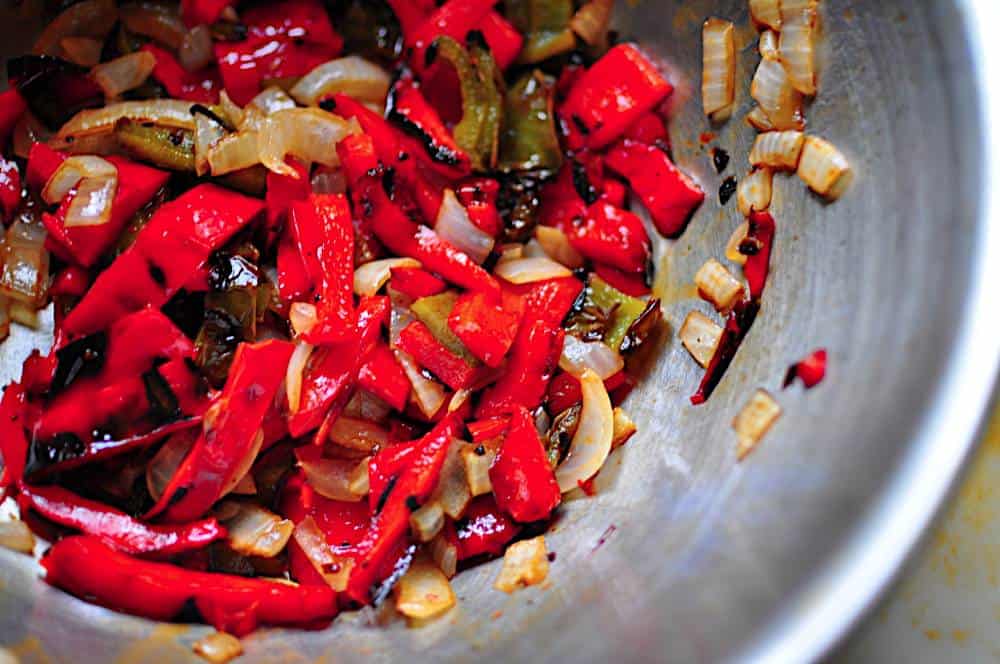 Finely diced red and green bell peppers and onion piled on a cutting board with a chef's knife