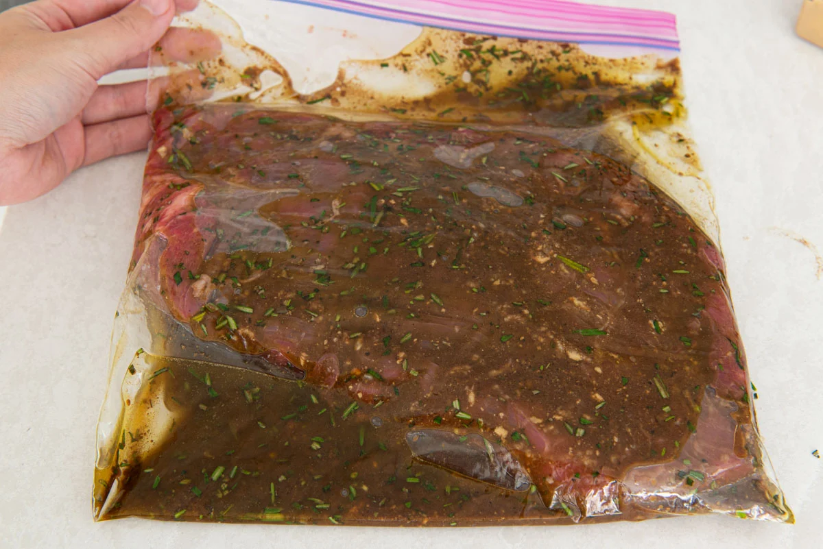 Flank steak marinating in a zip-top bag with visible lime juice, garlic, and spices on a kitchen counter