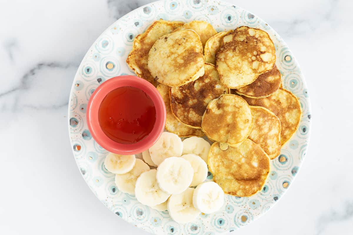 Flour, baking powder, egg, milk, banana, and vanilla arranged on a home kitchen counter with a mixing bowl nearby