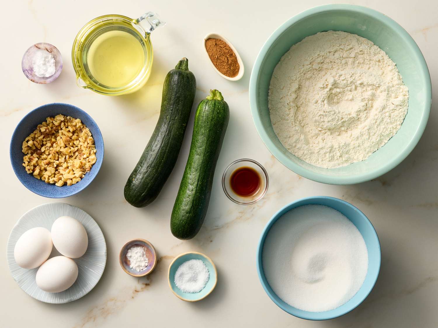 Flour, cocoa powder, sugar, chocolate chips, eggs, oil, and a whole zucchini arranged on a bright kitchen counter.
