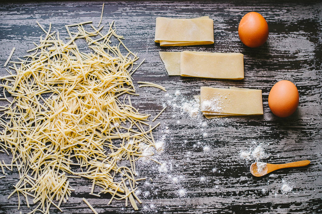 Flour, eggs, salt, and a small bowl of water arranged on a clean kitchen counter with a wooden rolling pin nearby