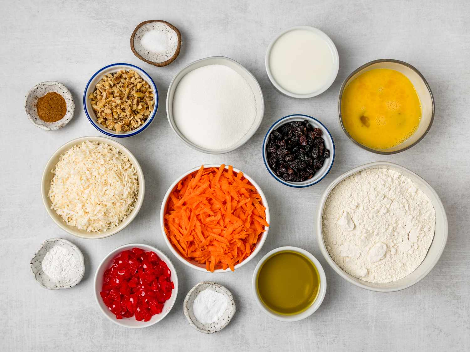Flour, eggs, shredded carrots, brown sugar, spices, oil, and a loaf pan arranged on a bright kitchen countertop