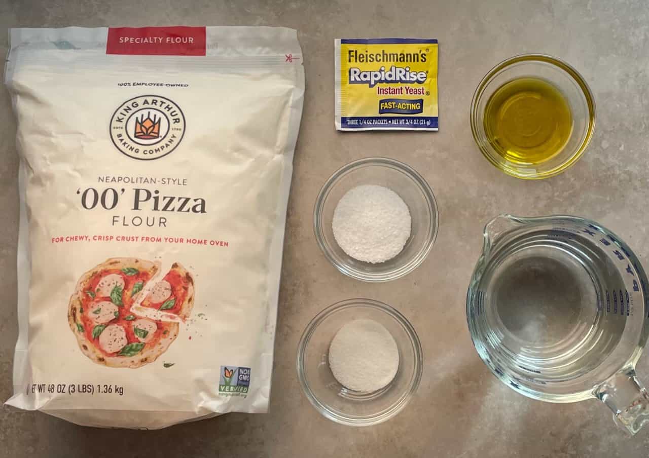 Flour, salt, yeast, sugar, olive oil, and water arranged on a bright kitchen countertop