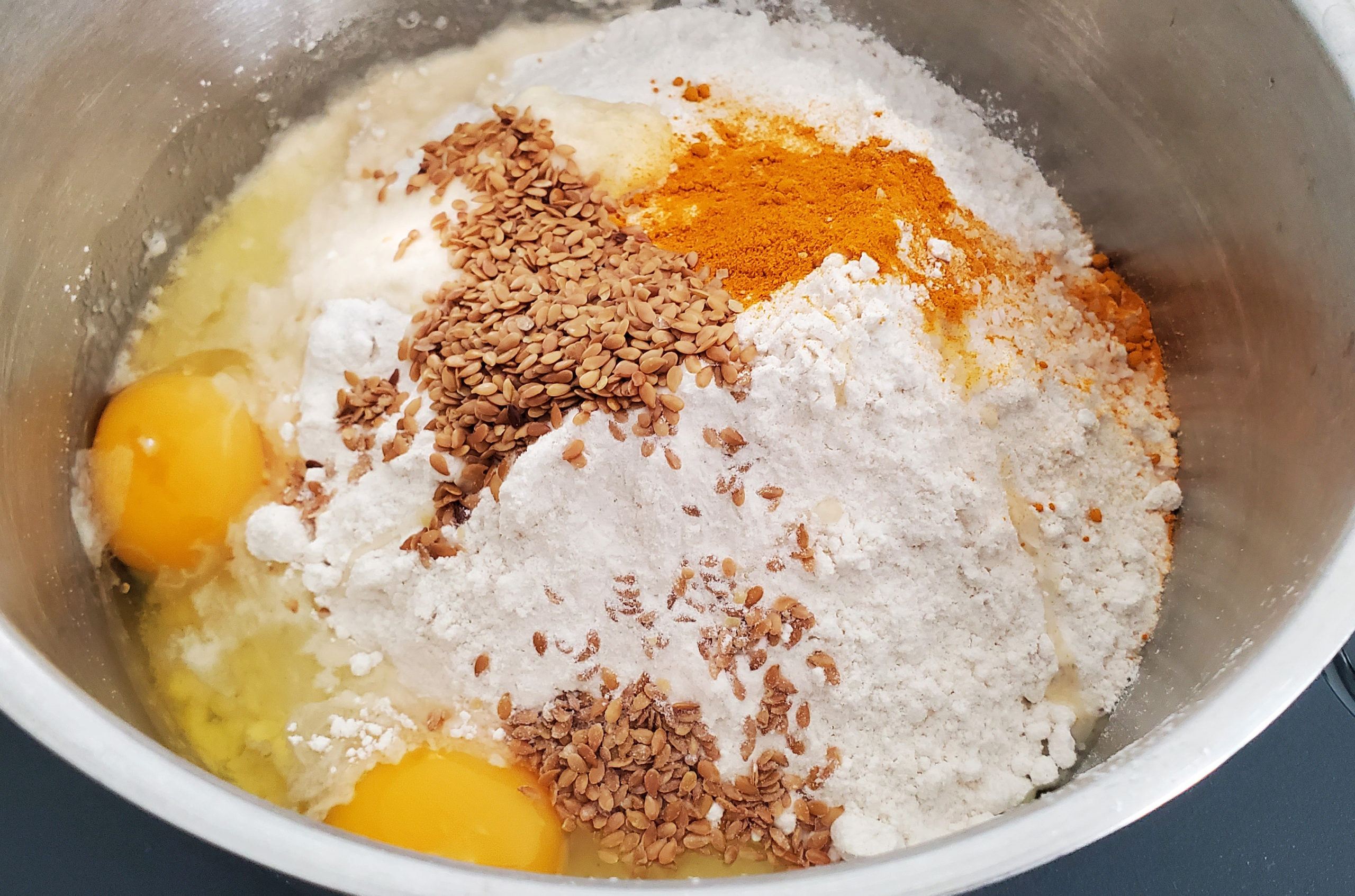 Flour, turmeric, curry powder, and cubes of cold butter in a mixing bowl on a kitchen counter, ready to be mixed into pastry dough
