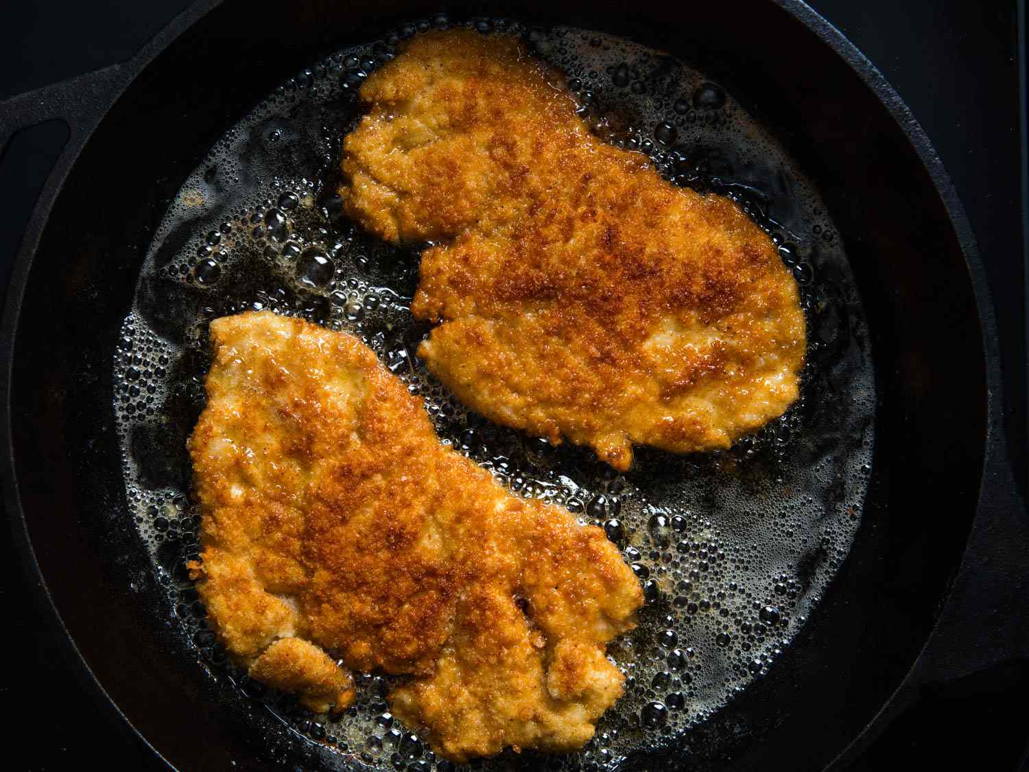 Floured chicken cutlets browning in a hot skillet with light golden edges forming