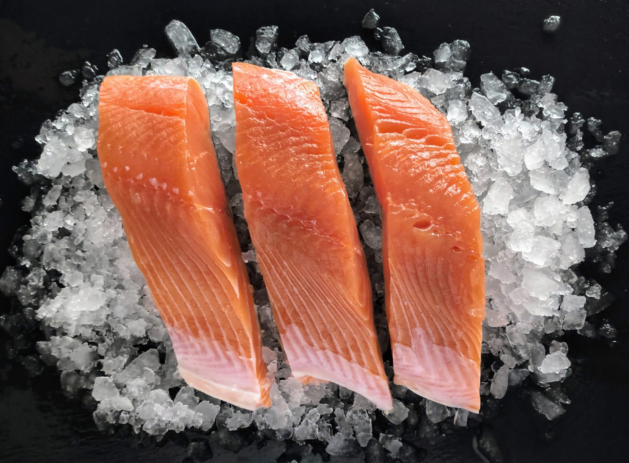 Four raw salmon fillets on a wooden cutting board with salt, pepper, and a small bowl of soy-honey ginger glaze nearby