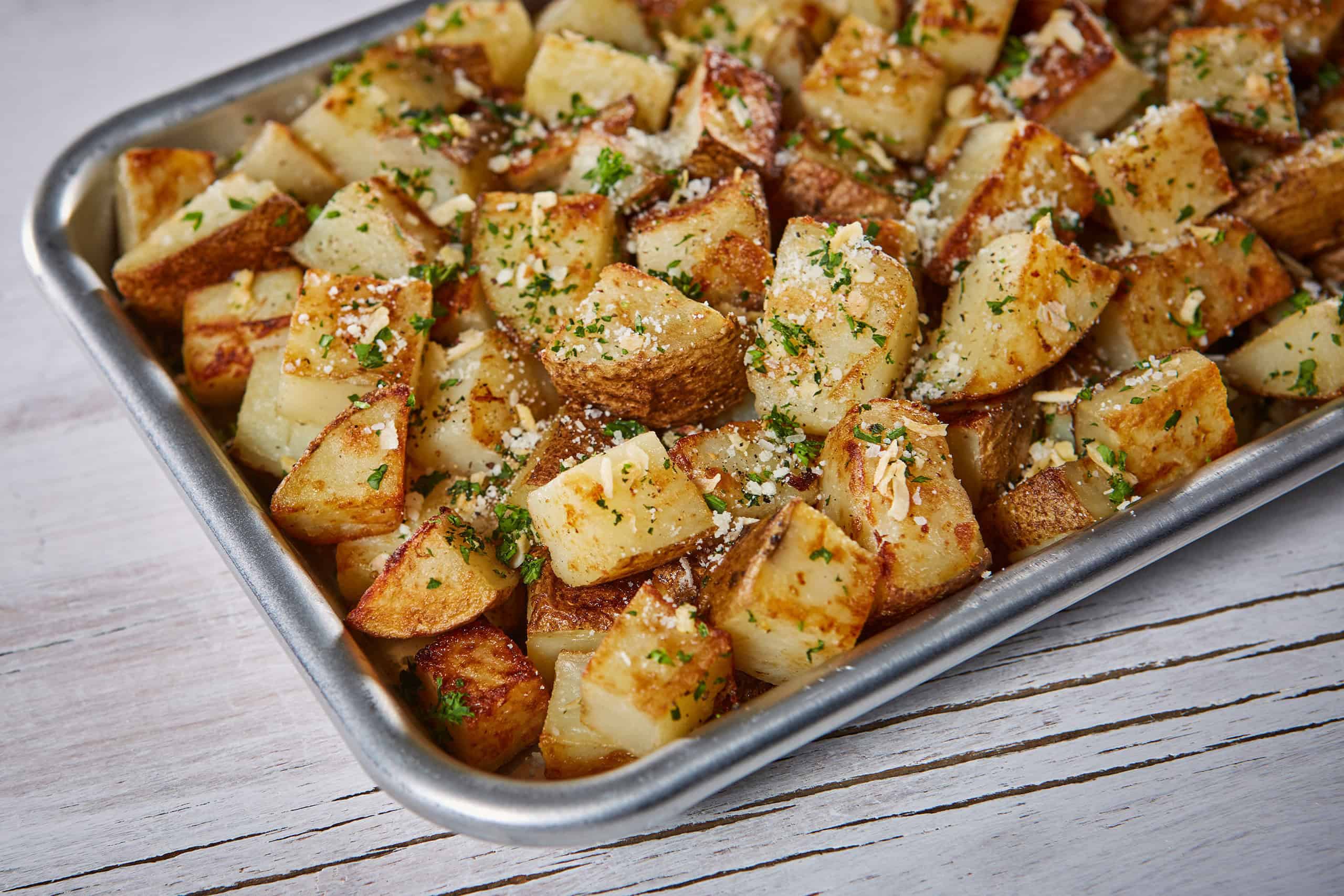 Four russet potatoes baking directly on the oven rack with crisped, lightly blistered skins, warm kitchen lighting