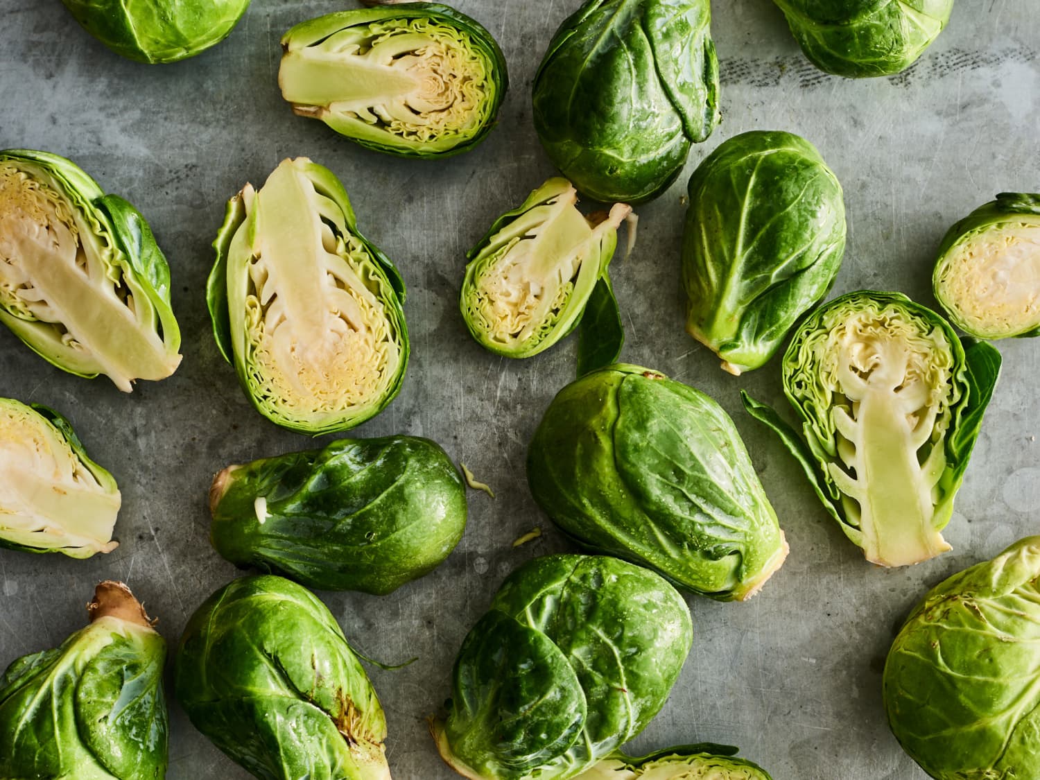 Fresh Brussels sprouts trimmed and halved on a wooden cutting board with a chef's knife nearby, bright kitchen counter lighting