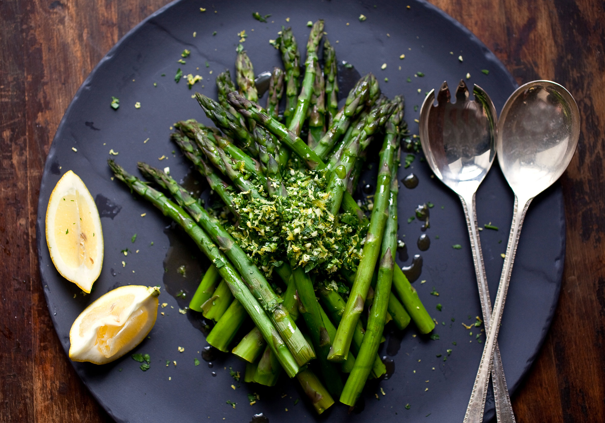 Fresh asparagus spears, olive oil, kosher salt, black pepper, lemon, and garlic arranged on a clean kitchen counter in natural light