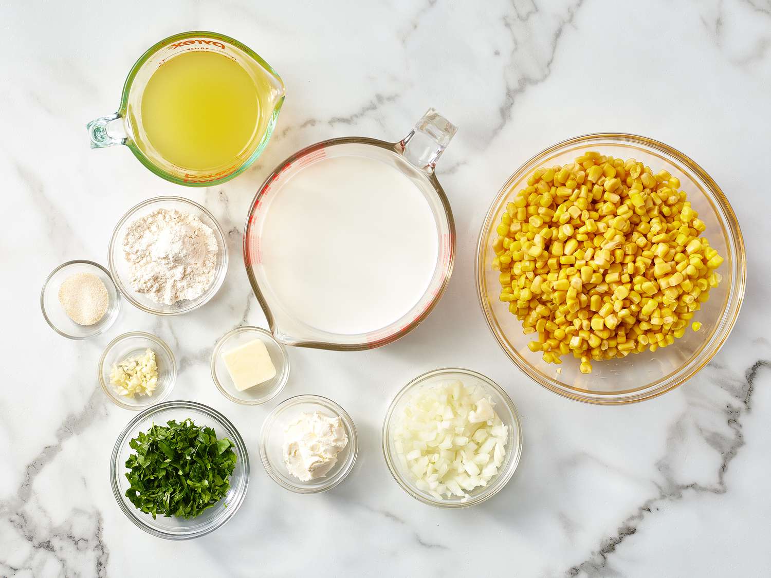 Fresh corn, onion, garlic, celery, potatoes, butter, broth, cream, and seasonings arranged on a bright kitchen counter