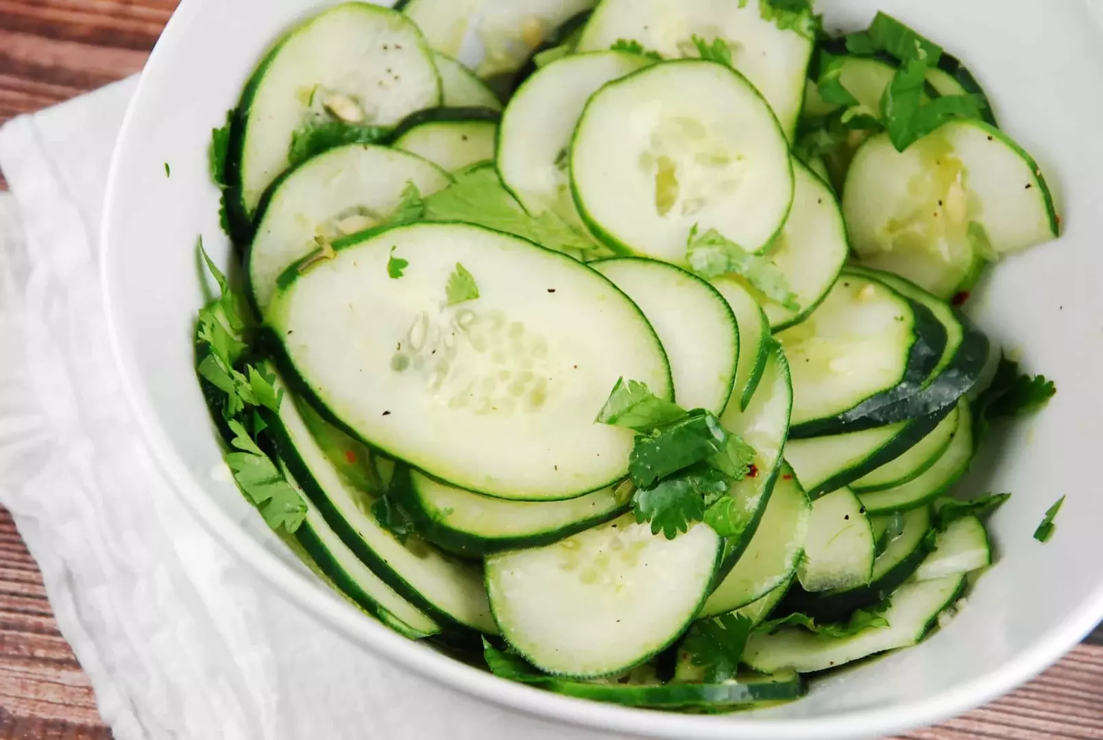 Fresh cucumbers, limes, cilantro, red onion, jalapeño, and a small bowl of spices arranged on a clean kitchen counter in natural light