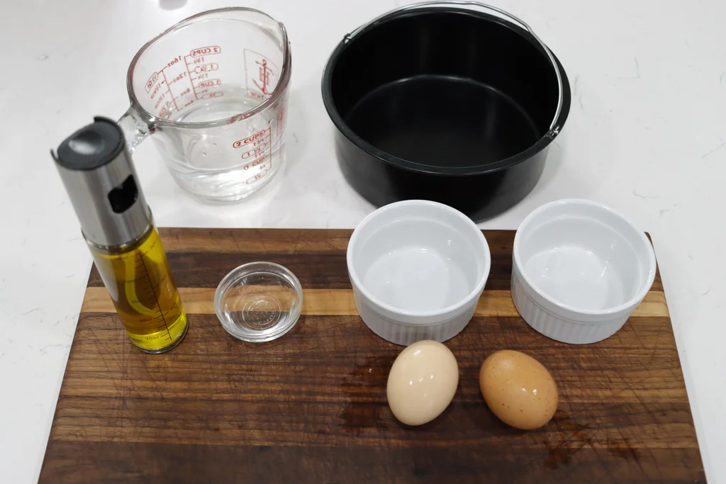 Fresh eggs, a small bottle of white vinegar, a pinch bowl of salt, and two small ramekins on a clean kitchen counter ready for poaching