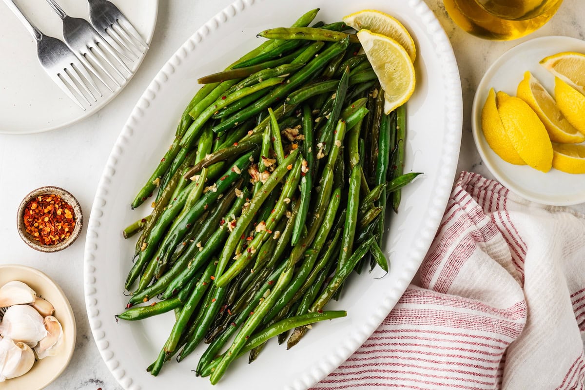 Fresh green beans, a lemon, garlic cloves, butter, and salt arranged on a counter