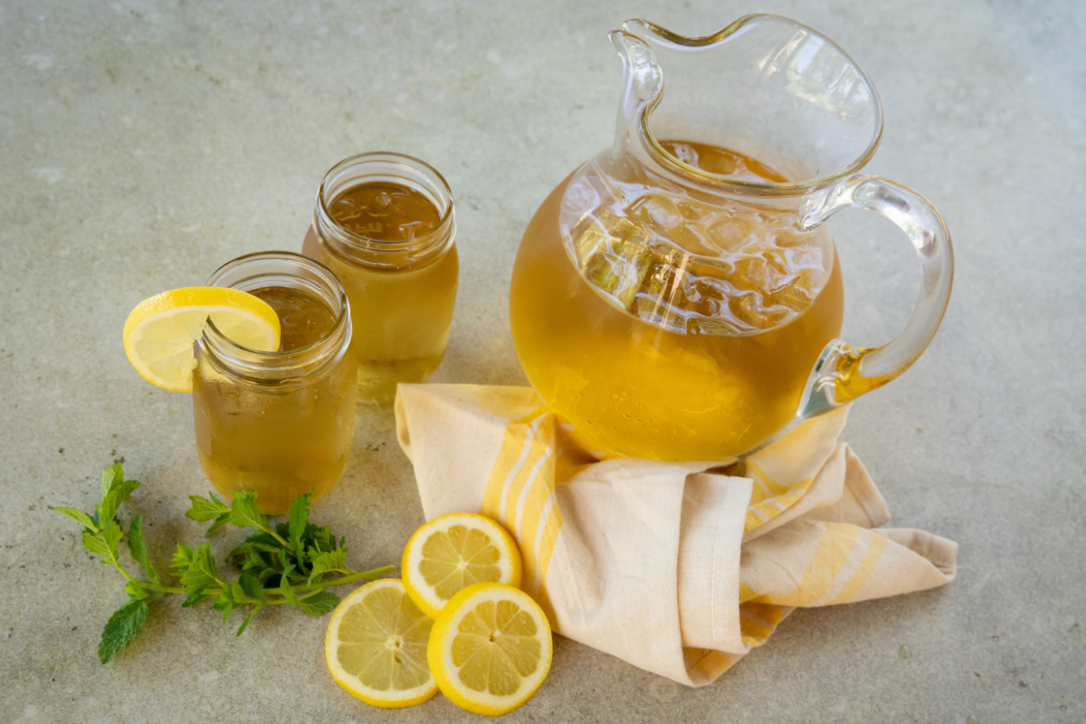 Fresh lemon balm leaves, a lemon, a small jar of honey, and a mug arranged on a bright kitchen counter