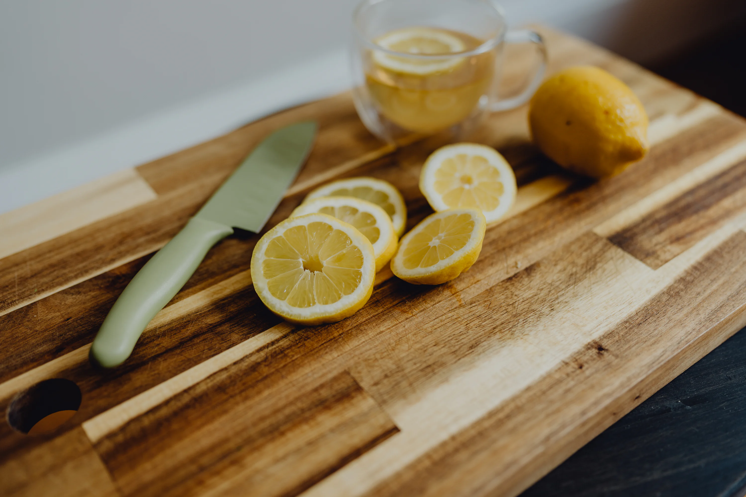 Fresh lemon slices on a cutting board next to a chef's knife on a bright kitchen counter