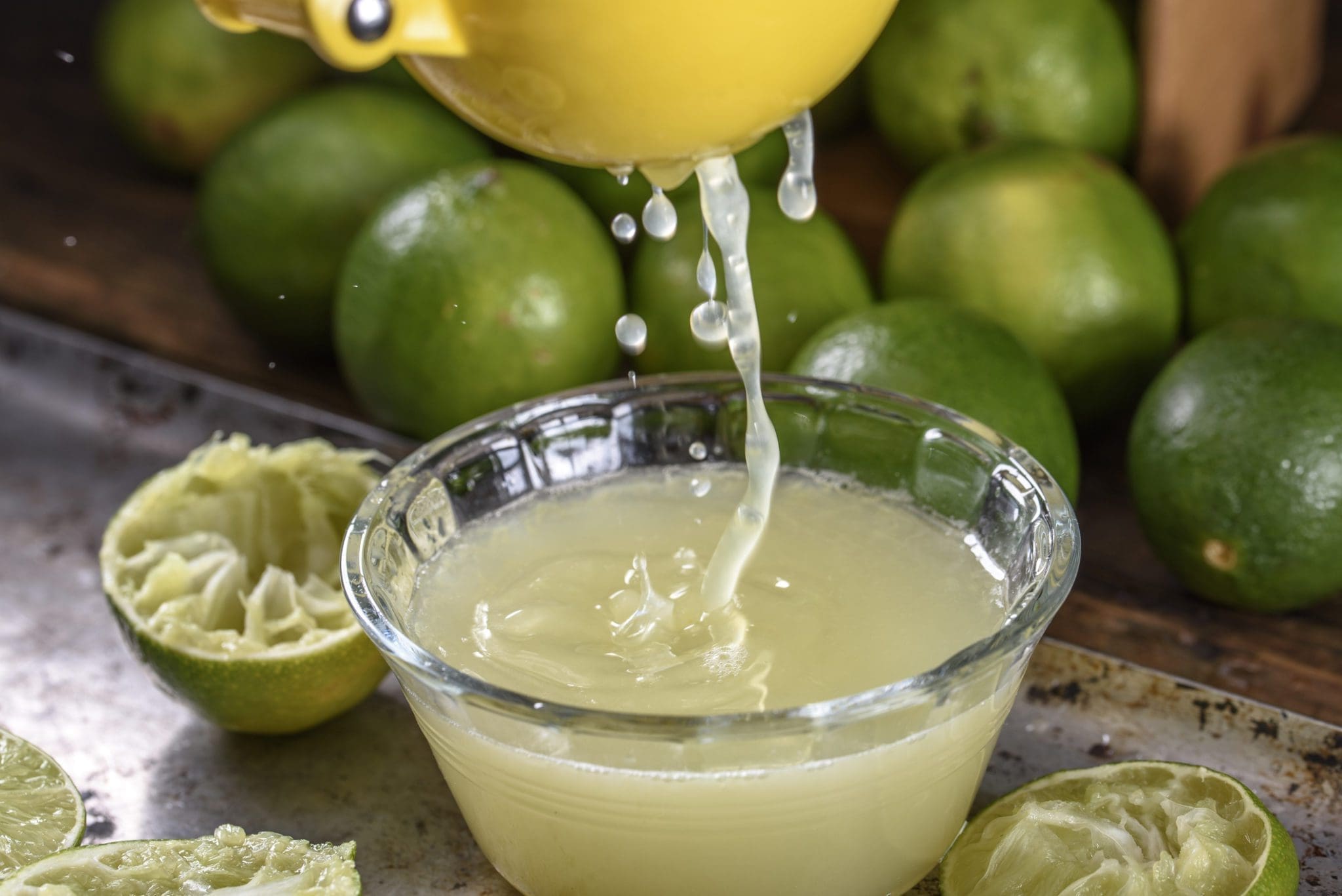 Fresh lime being juiced with a hand juicer on a kitchen counter, with a small bowl of cherries and a bottle of bitters nearby
