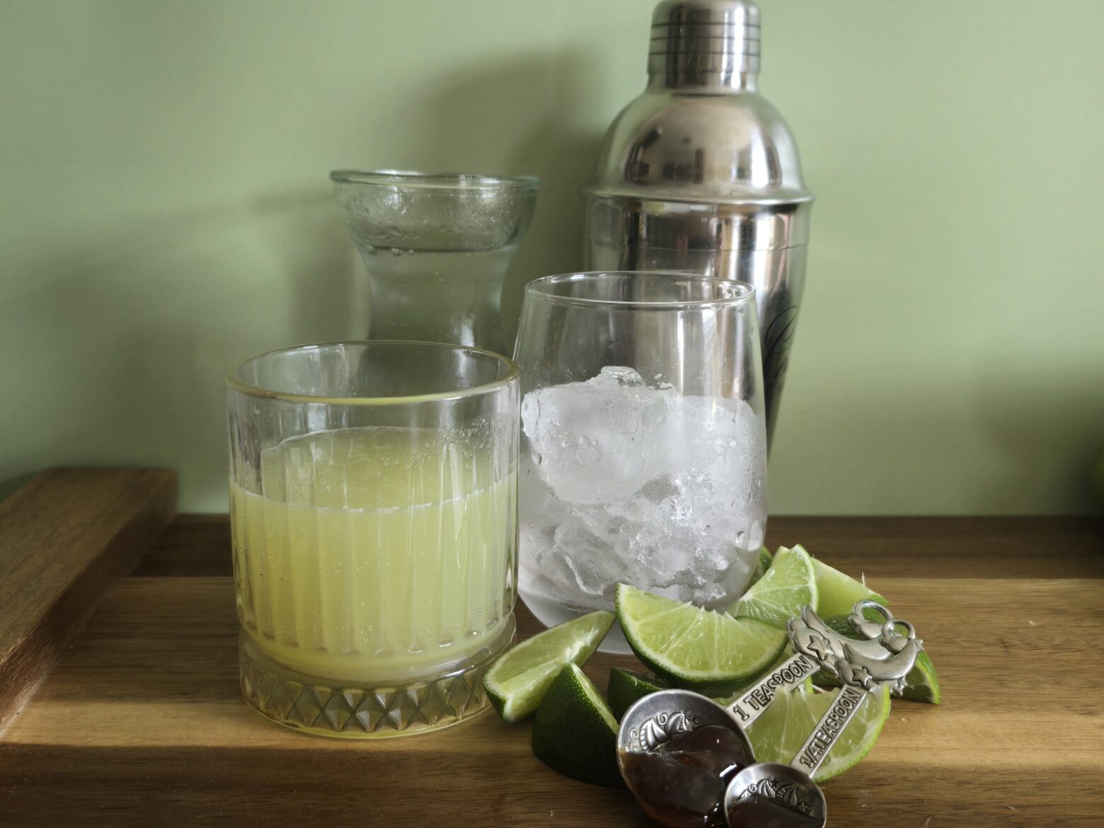 Fresh lime juice being added to a metal cocktail shaker on a kitchen counter with ice nearby