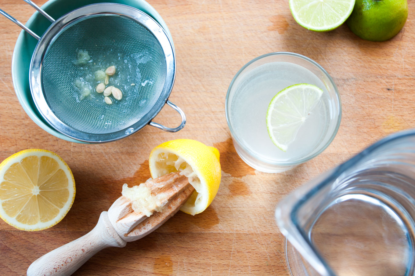 Fresh limes, a small bowl of sugar, and a glass measuring cup of water arranged on a tidy kitchen counter