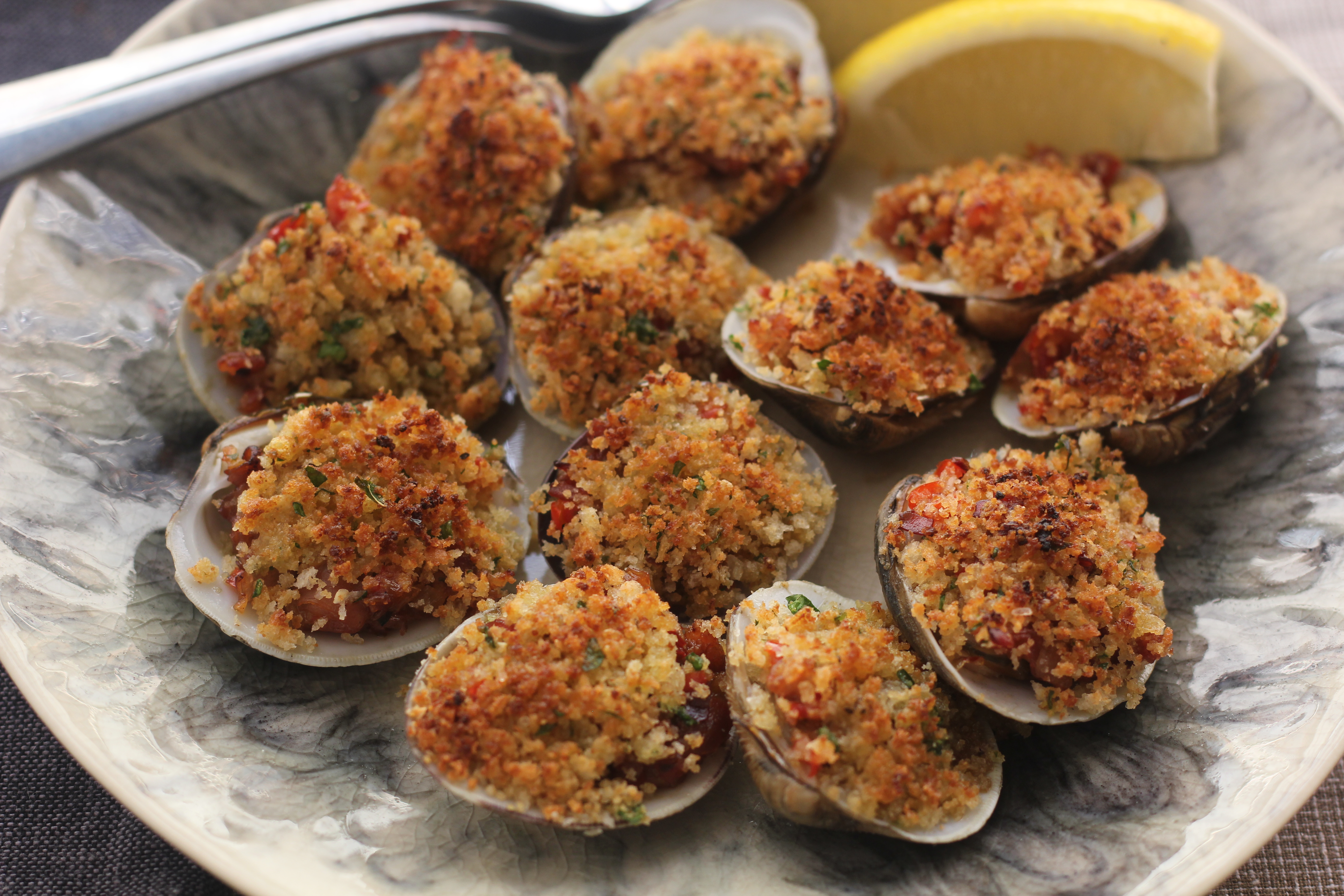 Fresh littleneck clams, bacon, bell pepper, celery, breadcrumbs, butter, lemon, and parsley arranged on a bright kitchen counter