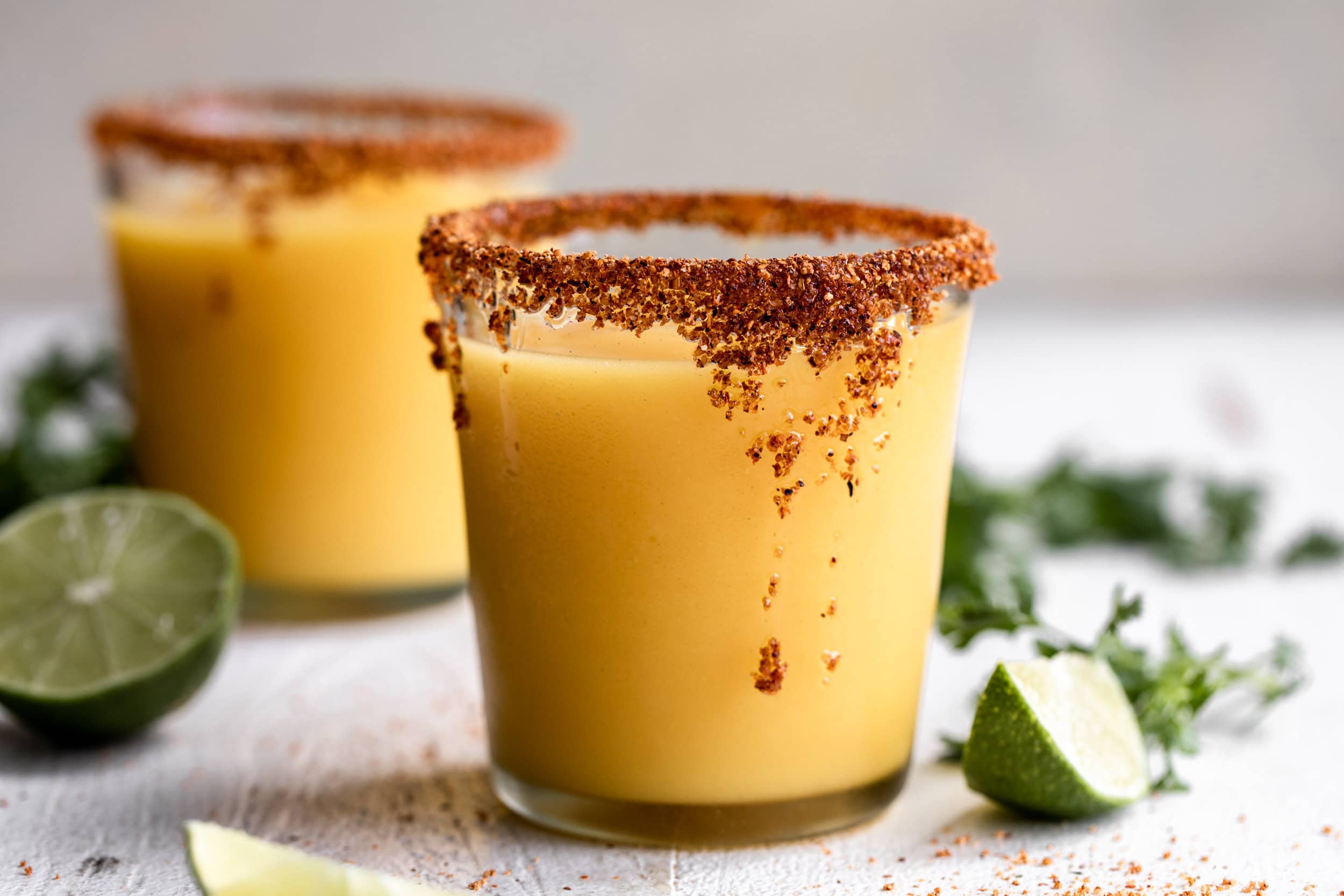 Fresh mango chunks, limes, tequila, orange liqueur, agave nectar, and a small bowl of chili-lime salt arranged on a clean kitchen counter