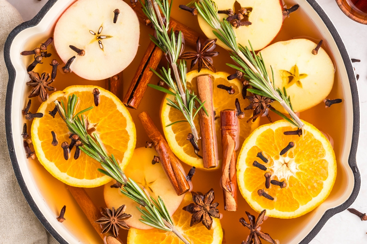 Fresh orange slices on a cutting board next to cinnamon sticks and whole cloves, ready to add to cider