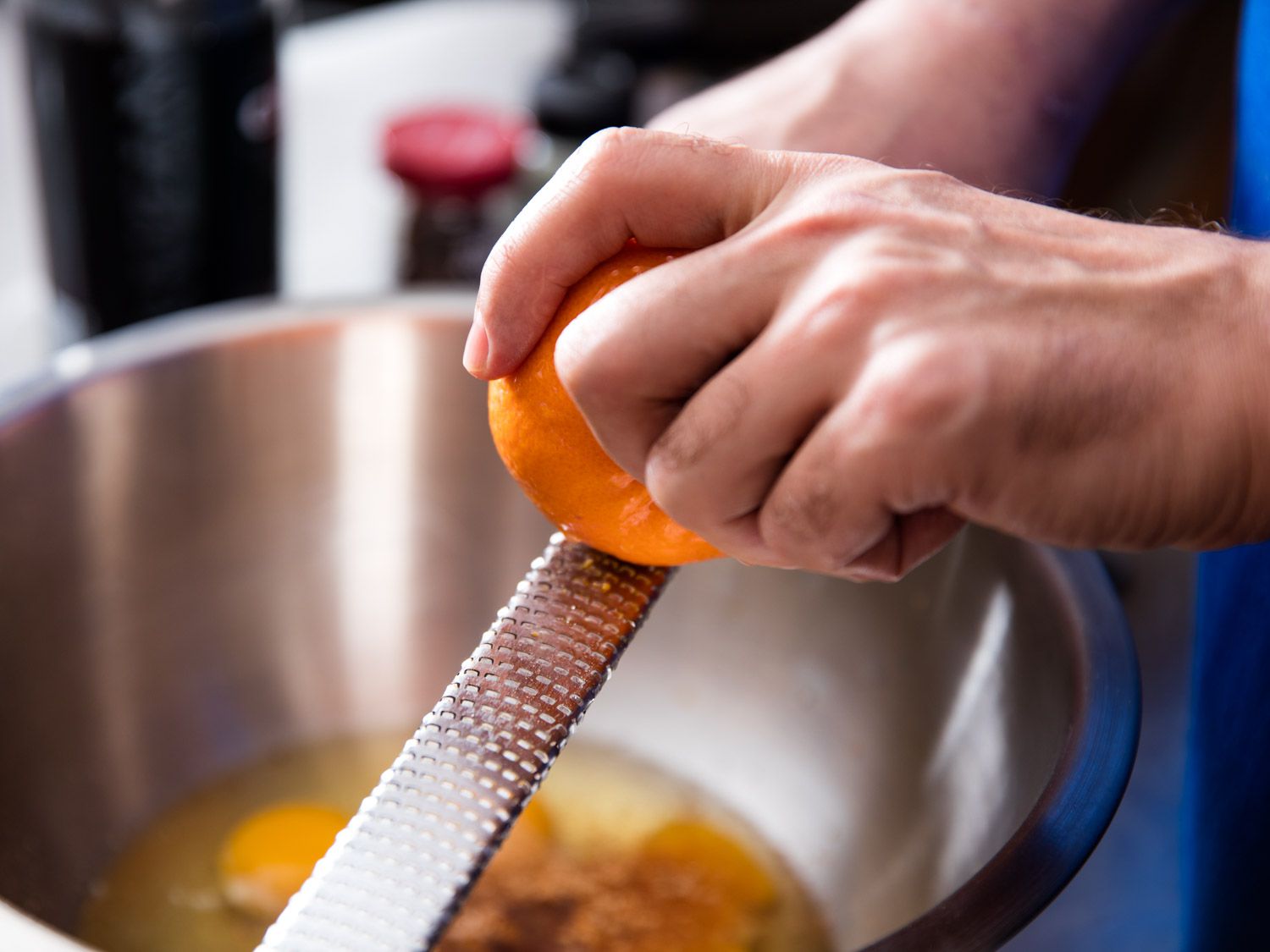Fresh oranges, a microplane, and a glass mixing bowl with orange zest on a clean kitchen counter