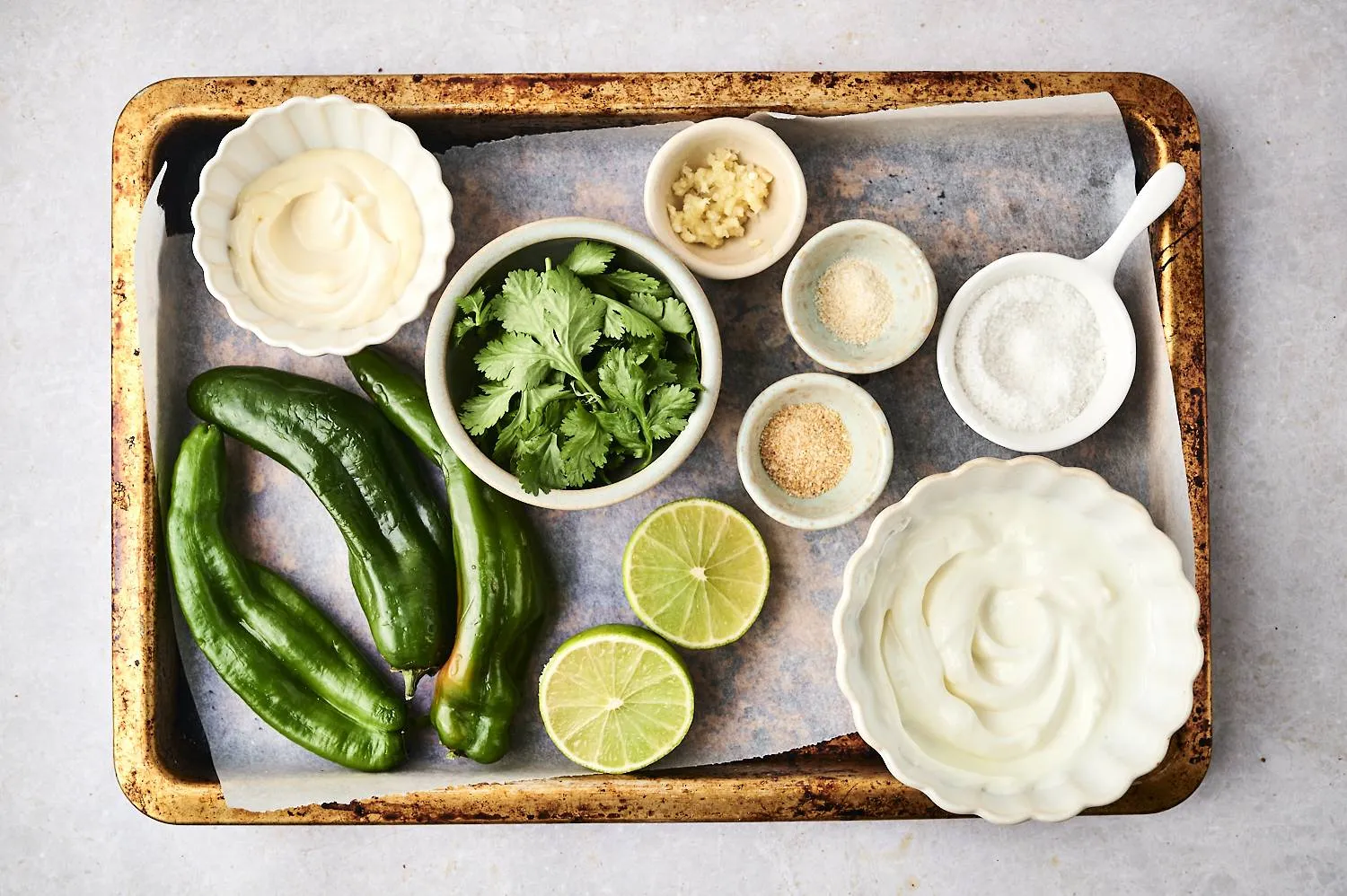 Fresh poblanos, cilantro, garlic, onion, lime, crema, and dry spaghetti arranged on a light stone kitchen counter in natural window light