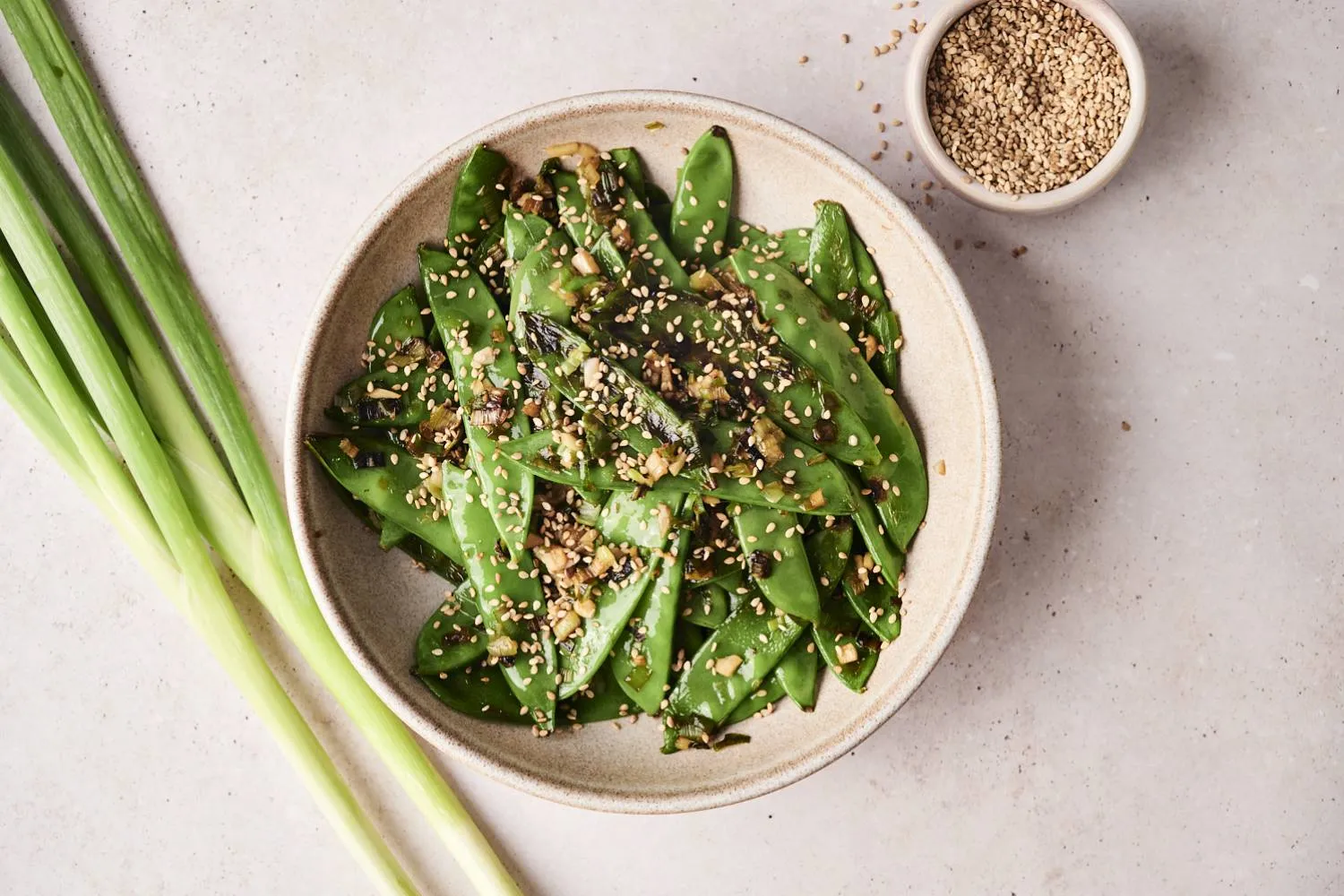 Fresh snow peas, garlic cloves, a small bowl of soy sauce, sesame oil, lemon, and cornstarch arranged on a clean kitchen counter in warm natural light