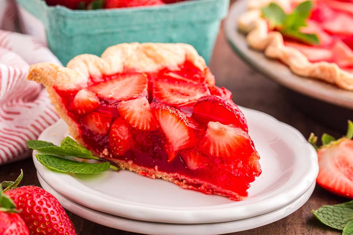 Fresh strawberries, a baked pie crust, sugar, cornstarch, and a box of strawberry gelatin arranged on a clean kitchen counter