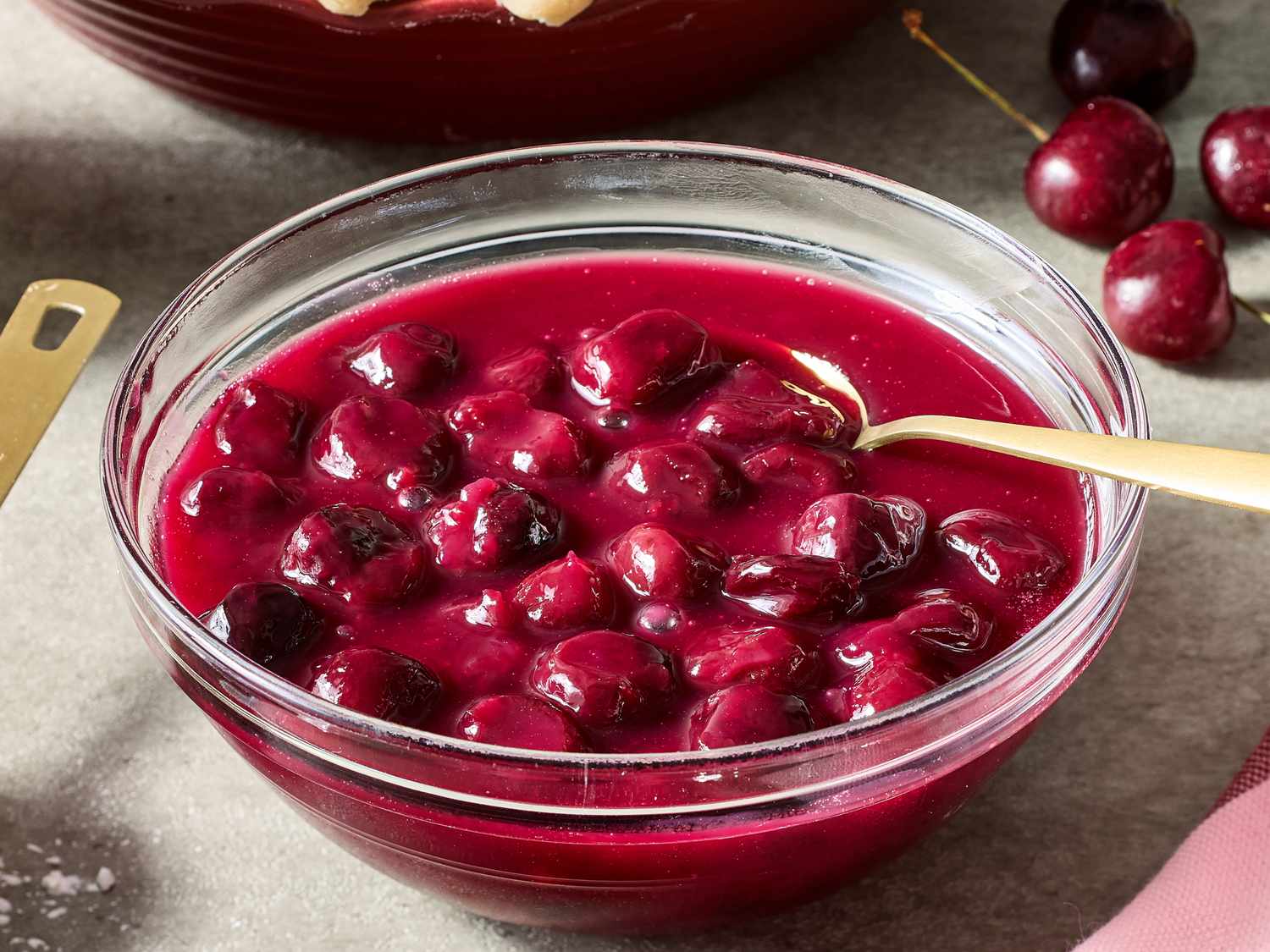 Fresh sweet cherries, granulated sugar, a lemon, and small bowls of cornstarch and salt arranged on a light kitchen counter