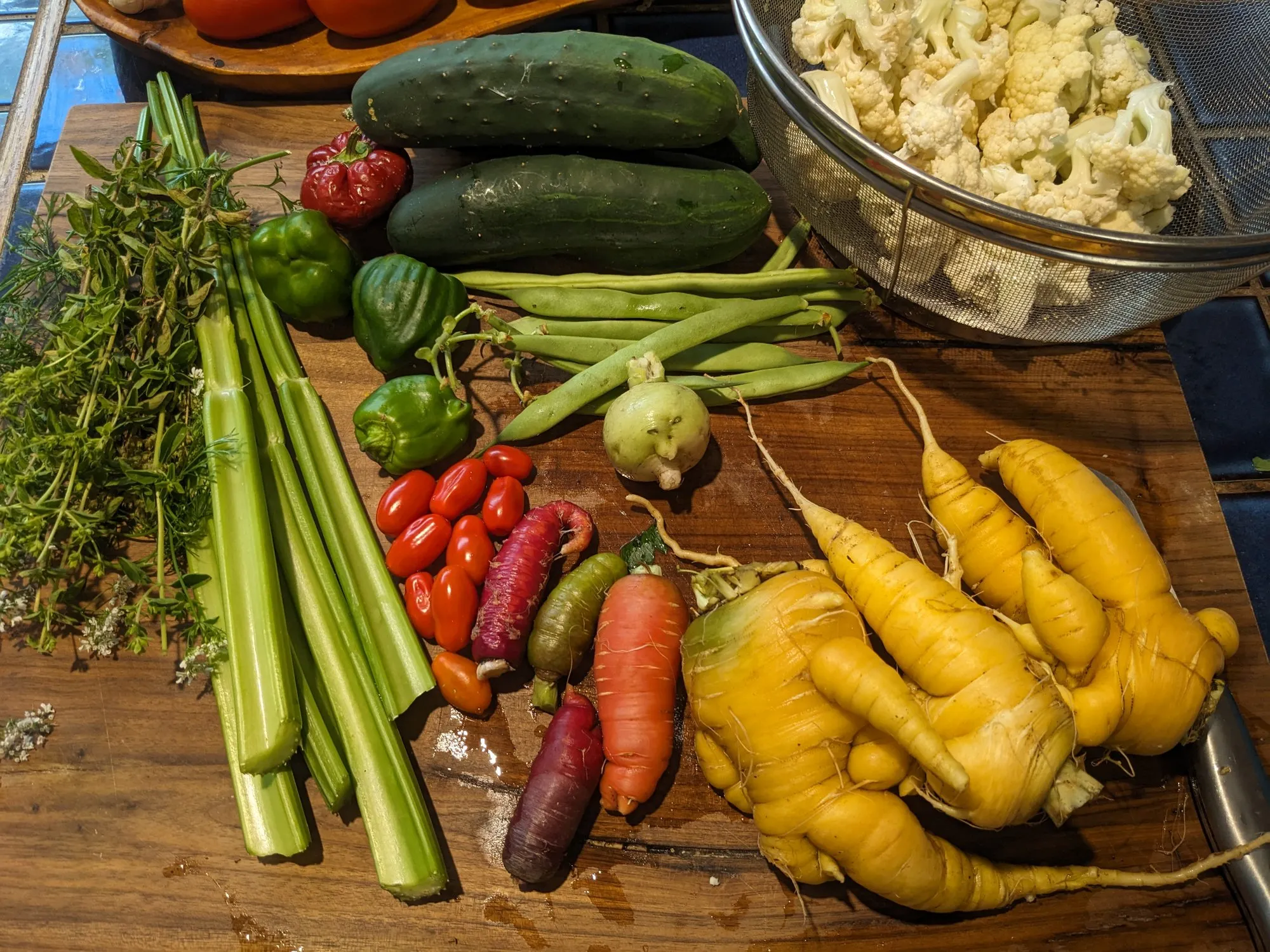 Fresh vegetables like cucumbers, carrots, radishes, and red onion sliced on a wooden cutting board with a chef's knife on a home kitchen counter