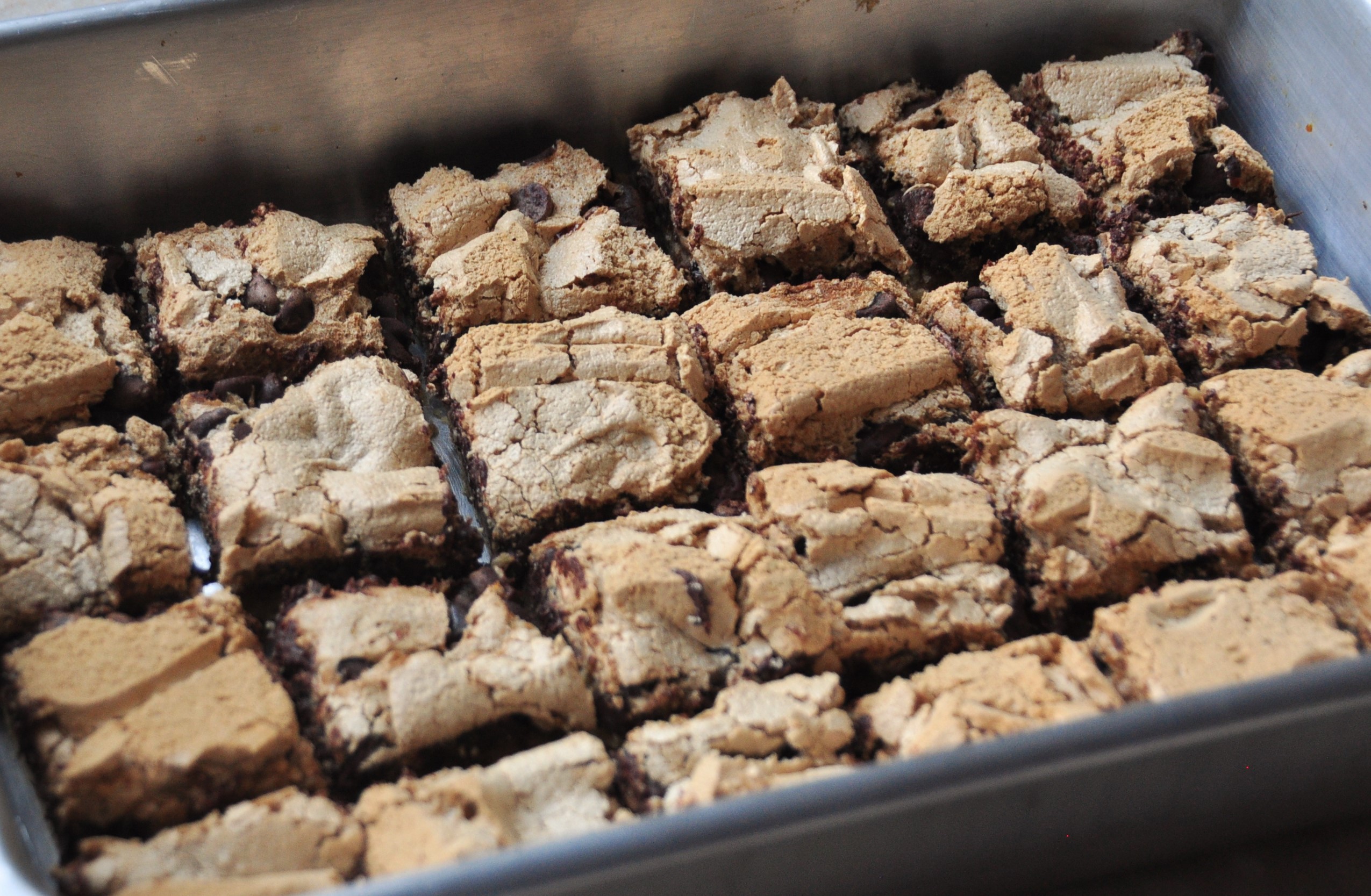 Freshly baked chocolate chip cookie bars in a metal baking pan on a light stone kitchen counter, golden edges and melty chocolate chips visible