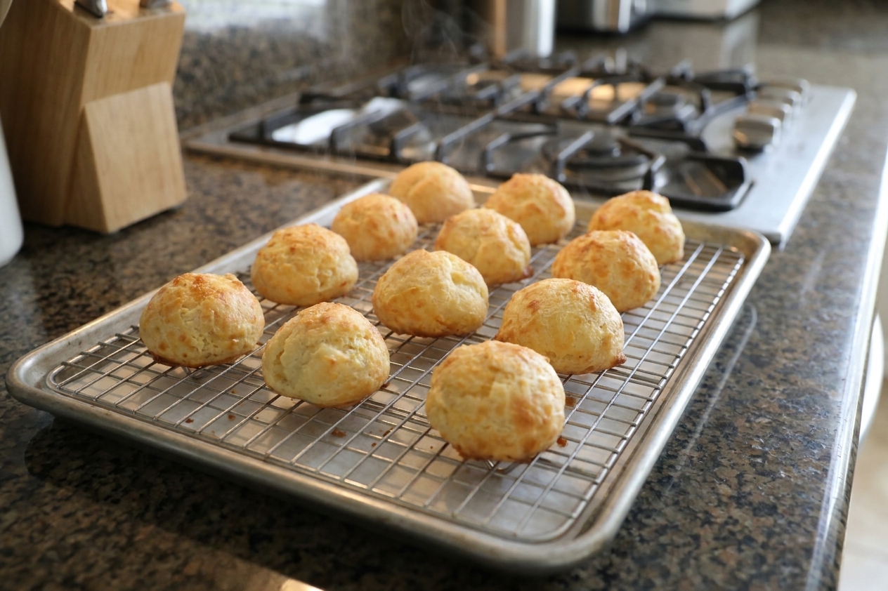 Freshly baked golden gougères cooling on a wire rack on a kitchen counter