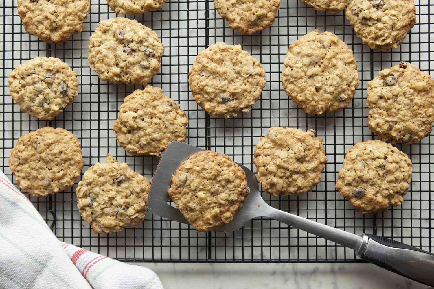 Freshly baked oatmeal cookies cooling on a wire rack with a sheet pan nearby in a warm home kitchen