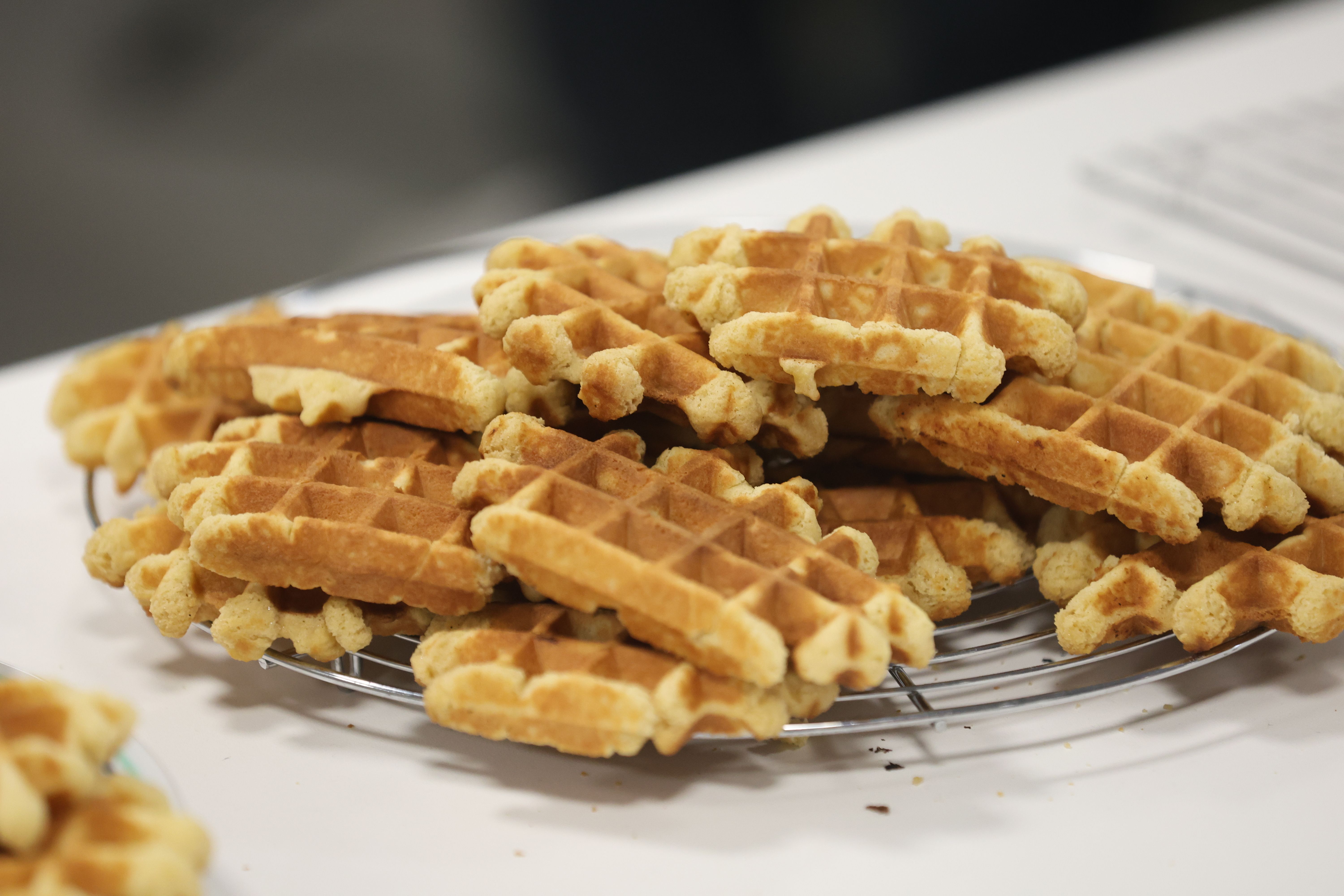 Freshly cooked pumpkin waffles cooling in a single layer on a wire rack set over a sheet pan on a kitchen counter