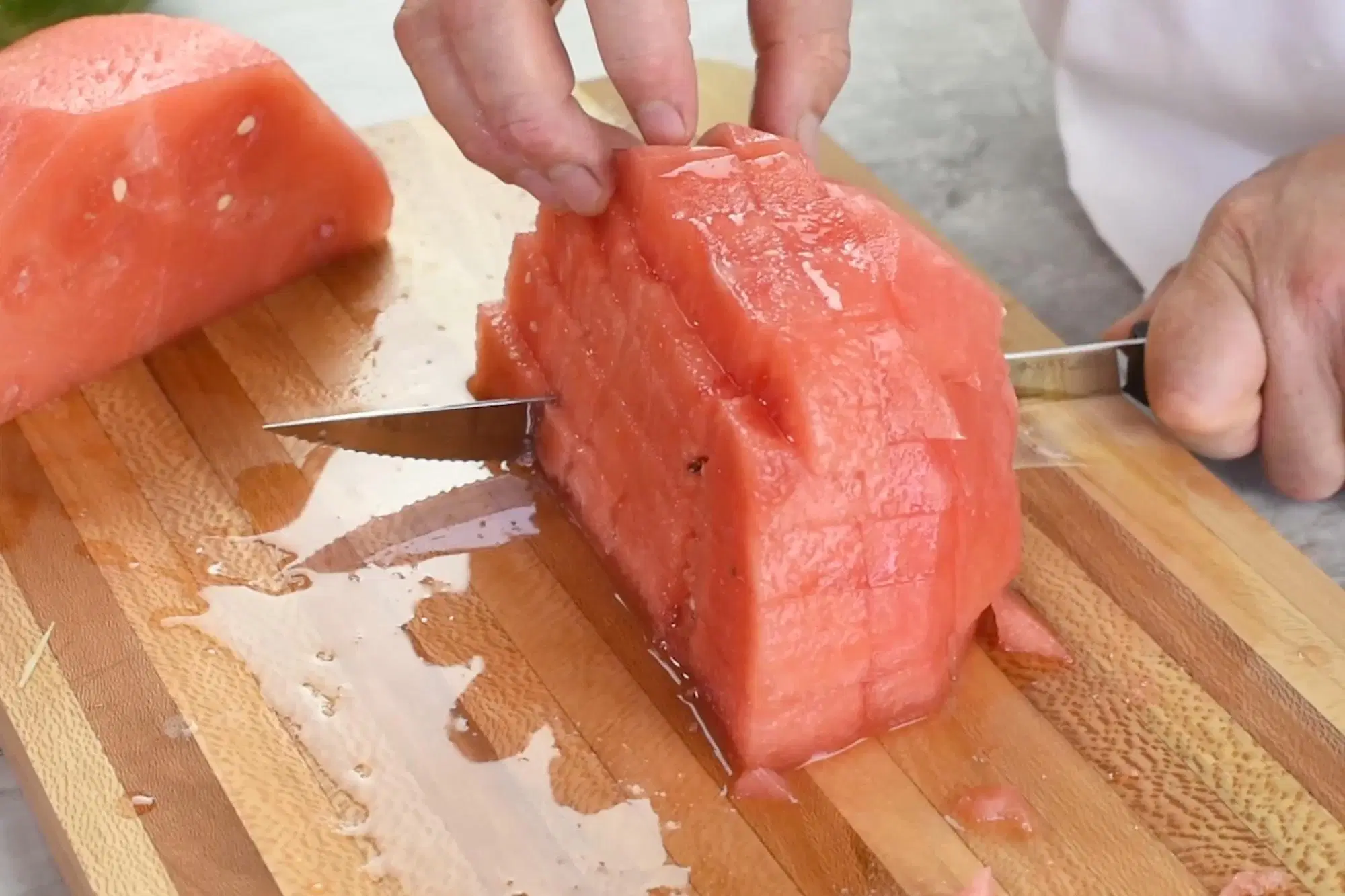 Freshly cubed watermelon piled on a wooden cutting board with a chef’s knife nearby on a bright kitchen counter